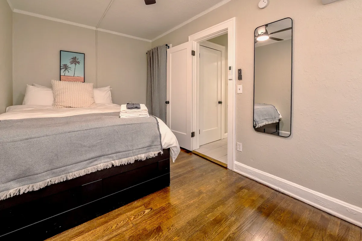A serene bedroom with a comfortable bed positioned near a mirror and a simple doorway. The space is filled with cozy, natural light, creating a peaceful atmosphere ideal for rest or preparing for the day.