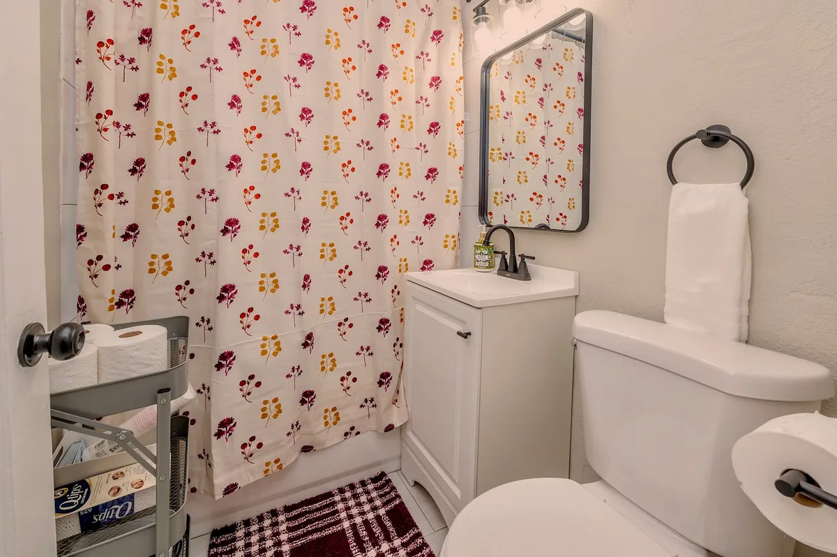 A modern bathroom scene with a cheerful floral shower curtain, a vanity with a sleek sink, and a well-lit mirror. The space is bright and welcoming, inviting moments of self-care and refreshment.