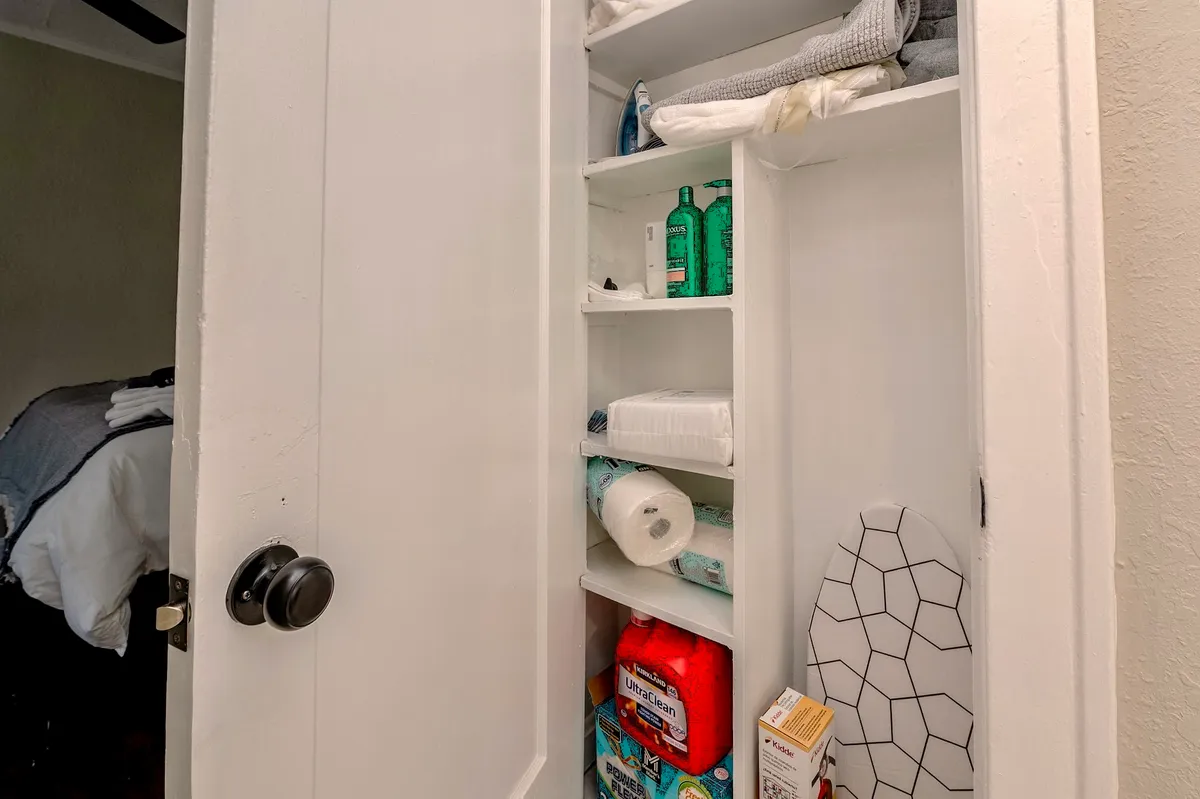 This image depicts shelves stacked with various household items, including cleaning supplies and an ironing board. The scene conveys an organized, tidy storage area within the apartment, highlighting the availability of practical amenities for residents.