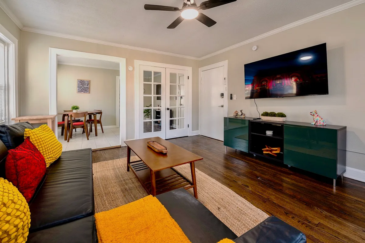 This image features a black leather sofa adorned with colorful throw pillows, paired with a wooden coffee table and a television unit. The scene is softly lit, suggesting ample natural light and a welcoming space for relaxing, watching TV, or socializing. The décor is modern yet cozy, with thoughtful details that contribute to a relaxing ambiance.
